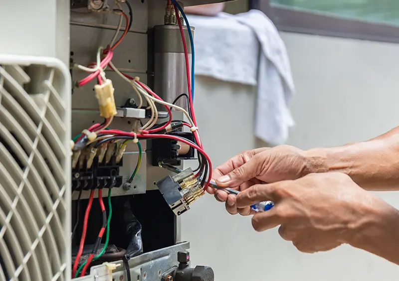 A person's hands repair complex wiring inside an electrical appliance using a small screwdriver.
