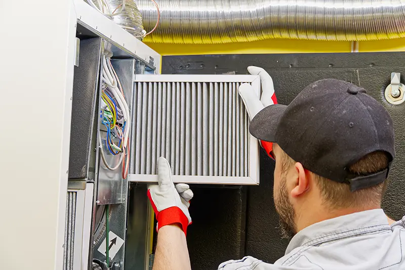 HVAC technician replacing a furnace air filter during furnace maintenance.
